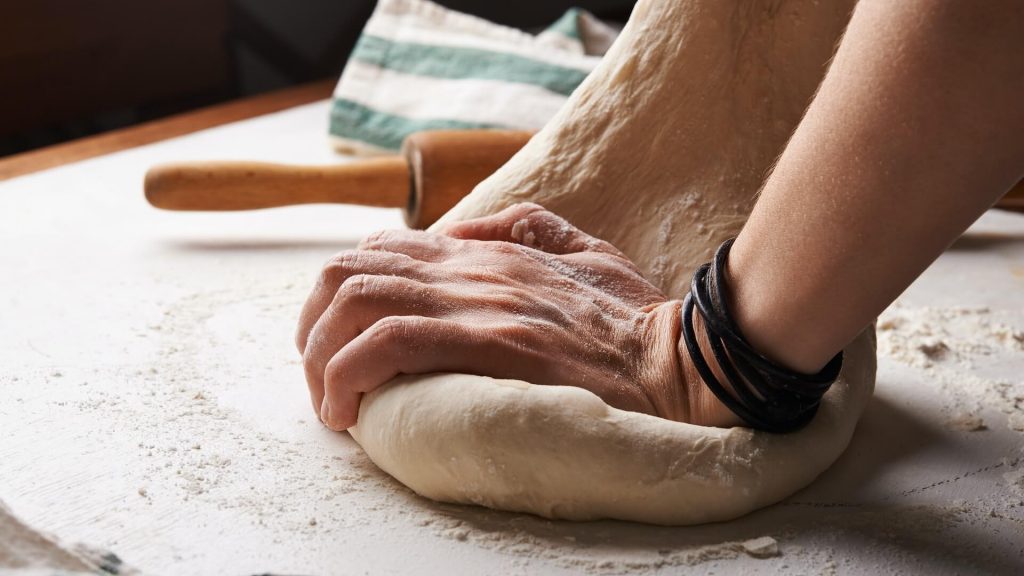 Les mains d'une personne pétrissant et façonnant habilement la pâte sur une surface farinée, la préparant pour la cuisson