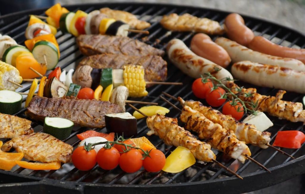 Un gril rempli d'une variété de viandes et de légumes en train de cuire, dégageant de délicieux arômes et présentant des marques de grillades carbonisées.