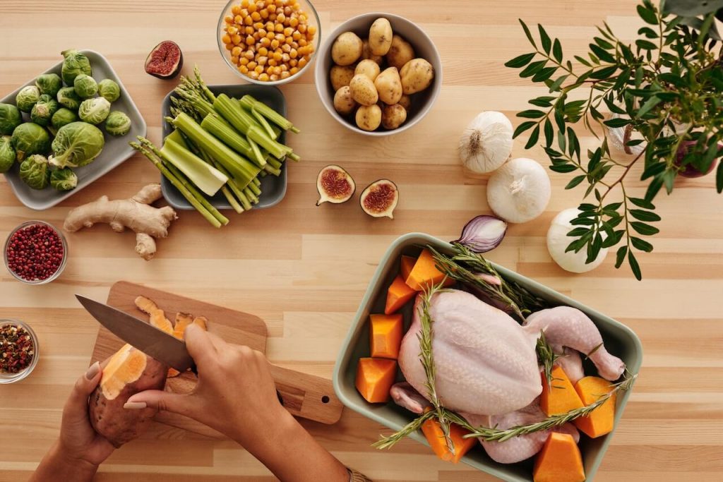 Une table sur laquelle se trouve un plateau contenant un poulet, entouré d'assiettes d'ingrédients frais, prêt pour la préparation d'un repas.